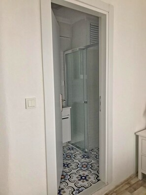 Ein schmales, geschlossenes Badezimmer mit einer Duschkabine aus Glas, einem weißen Waschbecken und Fliesen mit Muster.