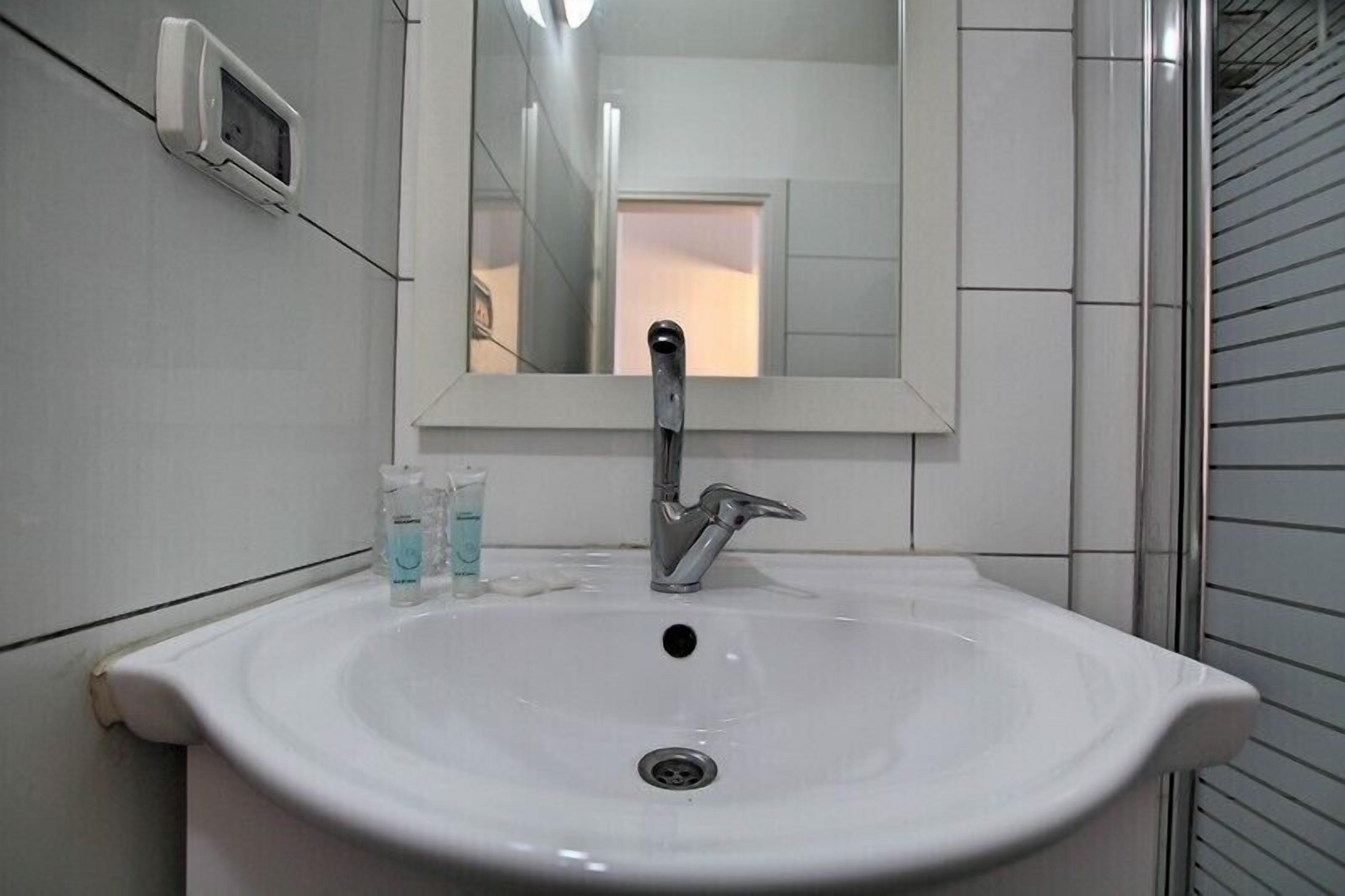 A white bathroom sink with a mirror above it, a faucet, and a soap dispenser.