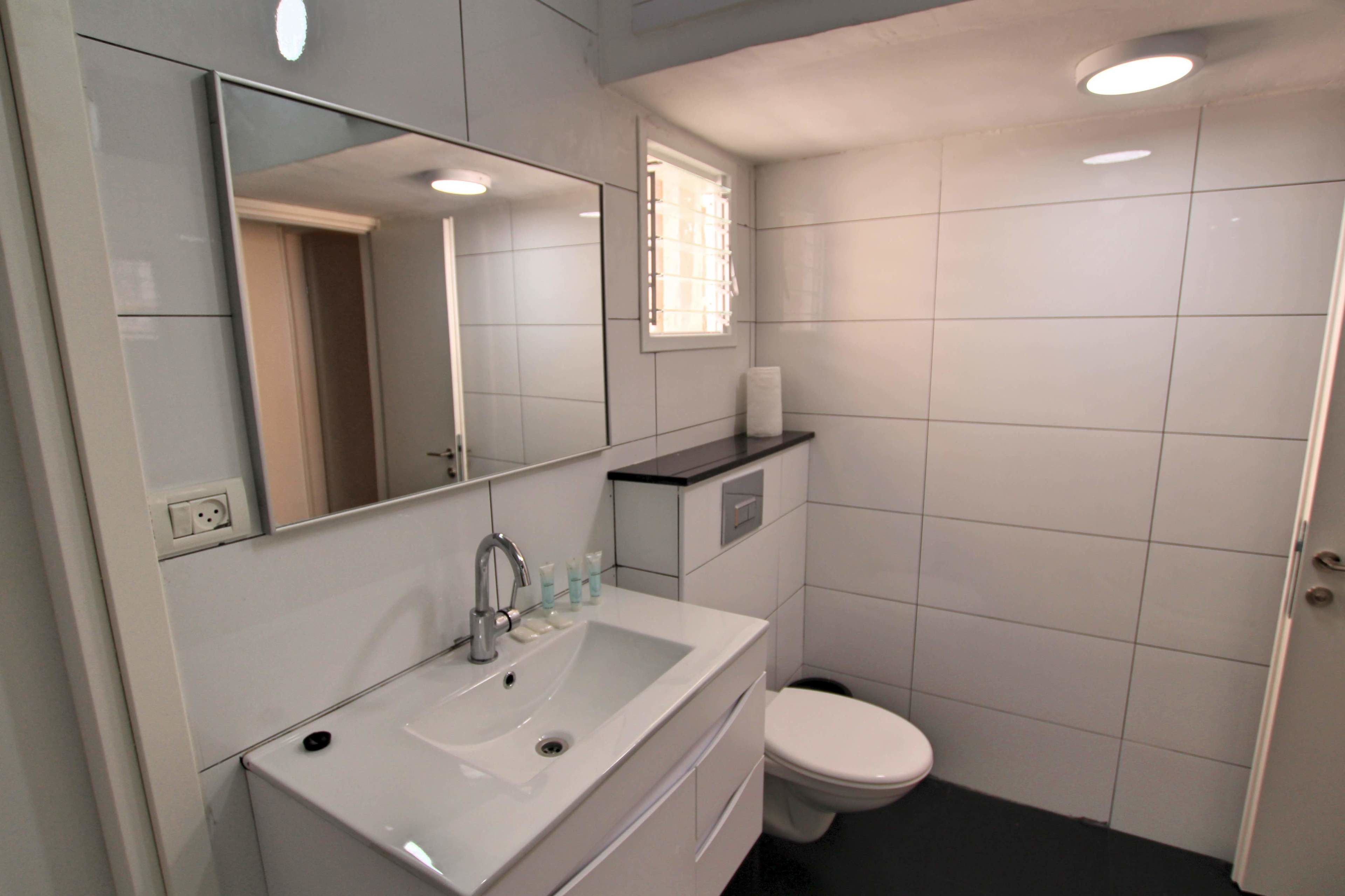 Un baño con lavamanos, espejo e inodoro blancos.