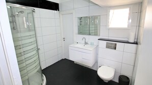 A modern bathroom with a glass-enclosed shower, a white sink with a mirror above it, and a toilet. - Arendalzrail Apartment - Balfour 35 (Bat Yam)