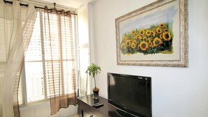 Une pièce avec un téléviseur posé sur un meuble en bois, une plante en pot et un tableau représentant des tournesols accroché au mur.