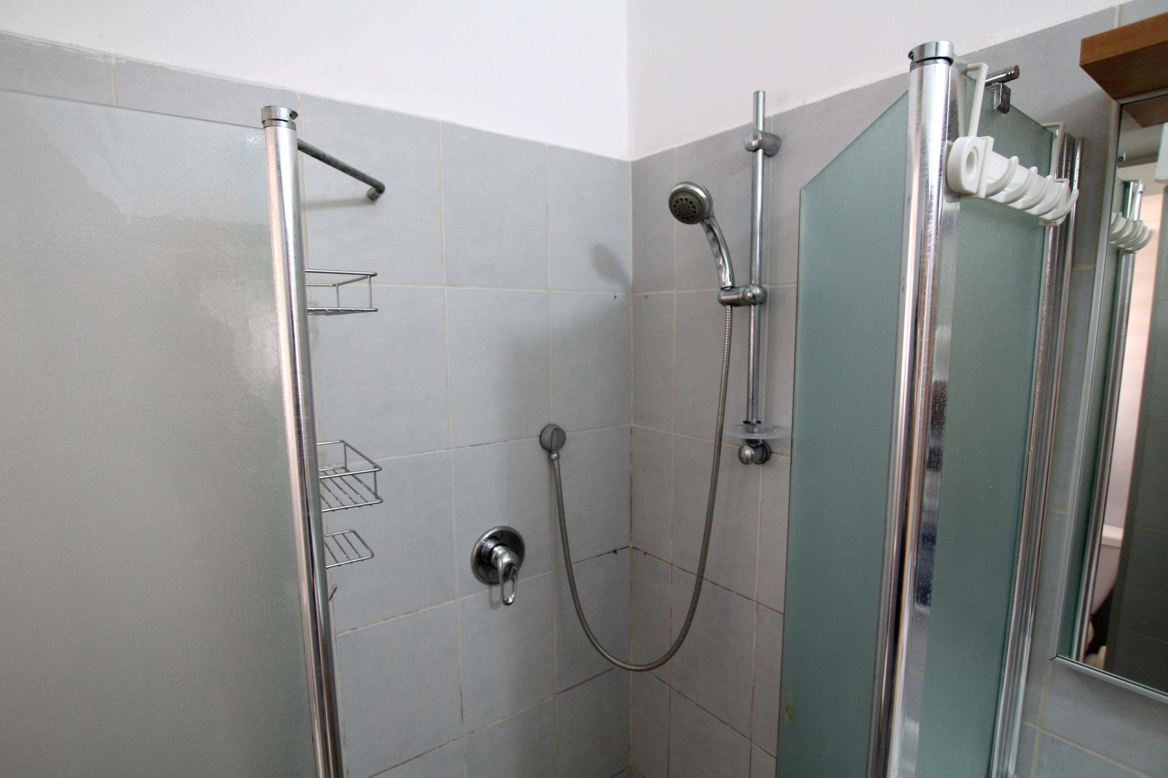 Una ducha con puerta de cristal, cabezal de ducha de mano y grifo empotrado.