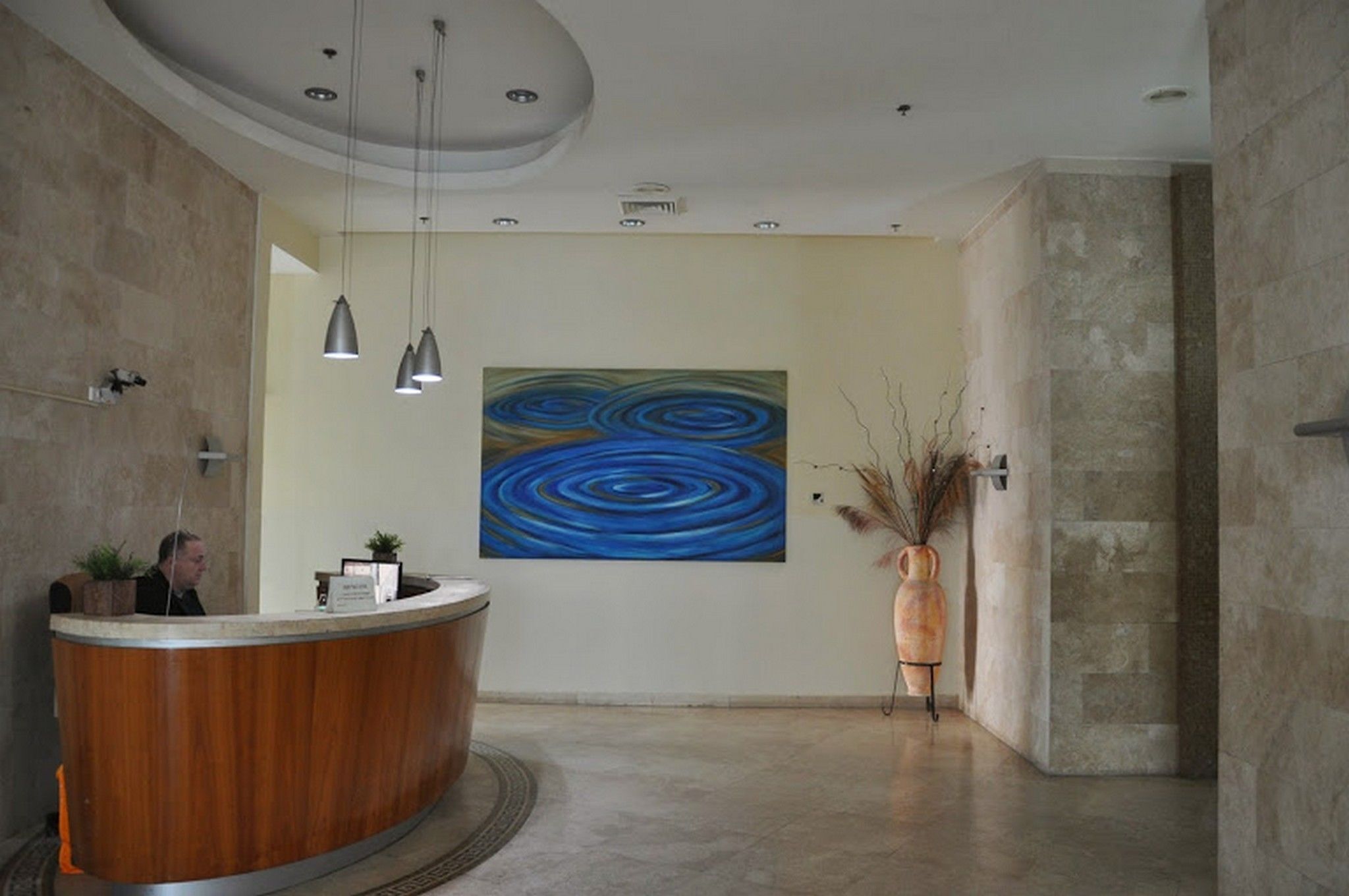 Un área de recepción con un mostrador de madera, un cuadro abstracto grande en la pared y un jarrón con plantas secas.
