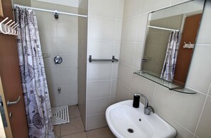 A bathroom with a shower, a sink, a glass shelf, and a mirror. - Arendalzrail Apartments - Yoseftal Street 3 (Bat Yam)