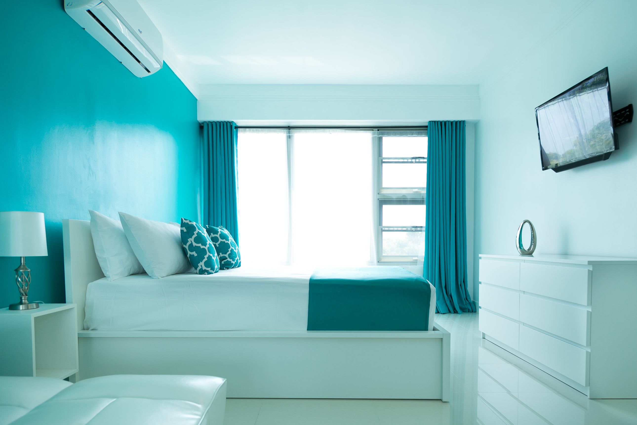 Ein Schlafzimmer mit Bett, Kommode, Fernseher und einem Fenster mit Vorhängen.
