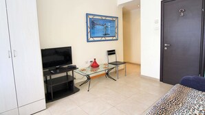 Una habitación con una mesa de vidrio, un televisor, un florero rojo y un cuadro en la pared.