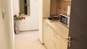 Un pasillo estrecho con piso de baldosas, una pequeña cocina con microondas y estufa, y un florero con flores rojas a la izquierda.