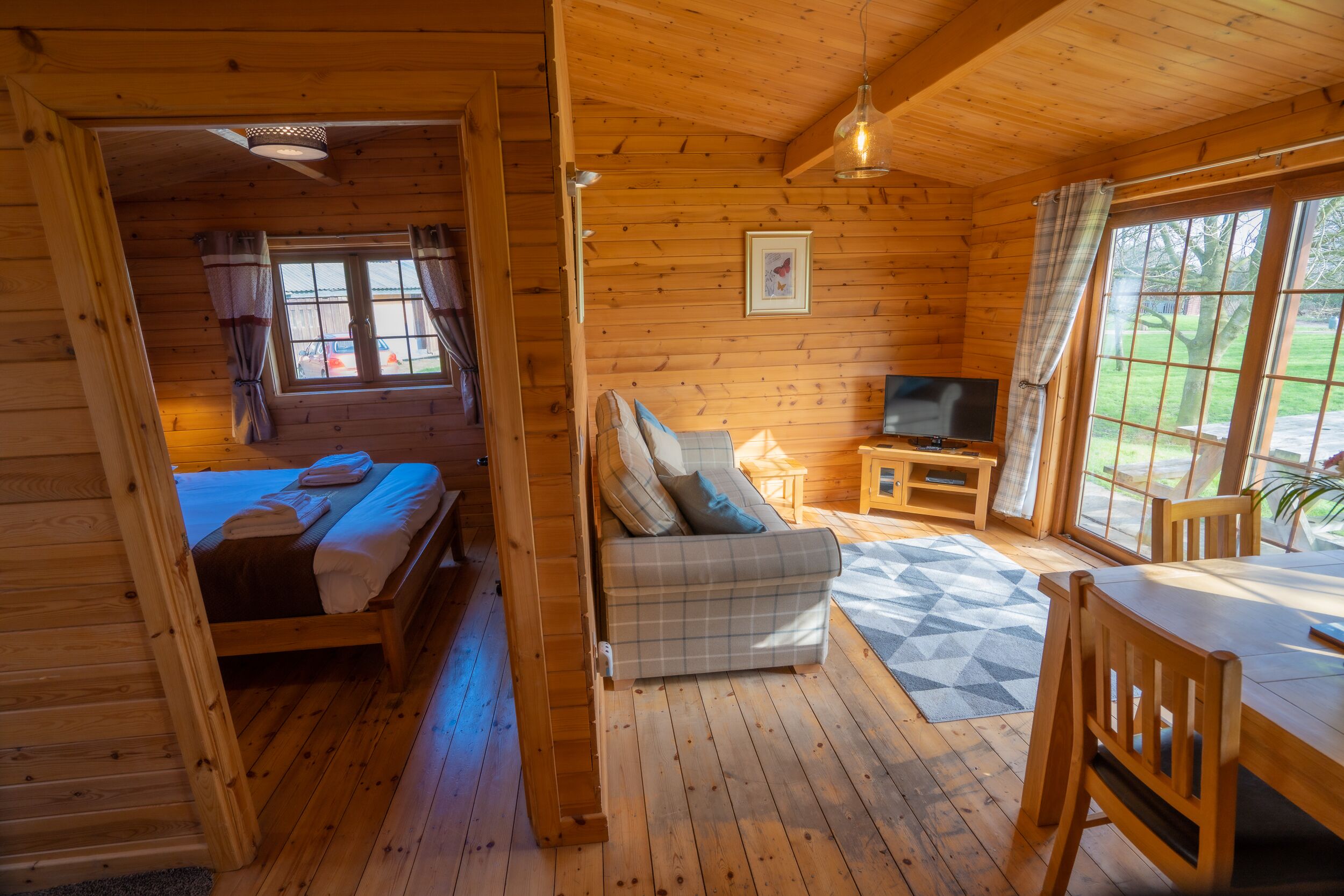 A wooden cabin interior with a bed, sofa, TV, and dining area.