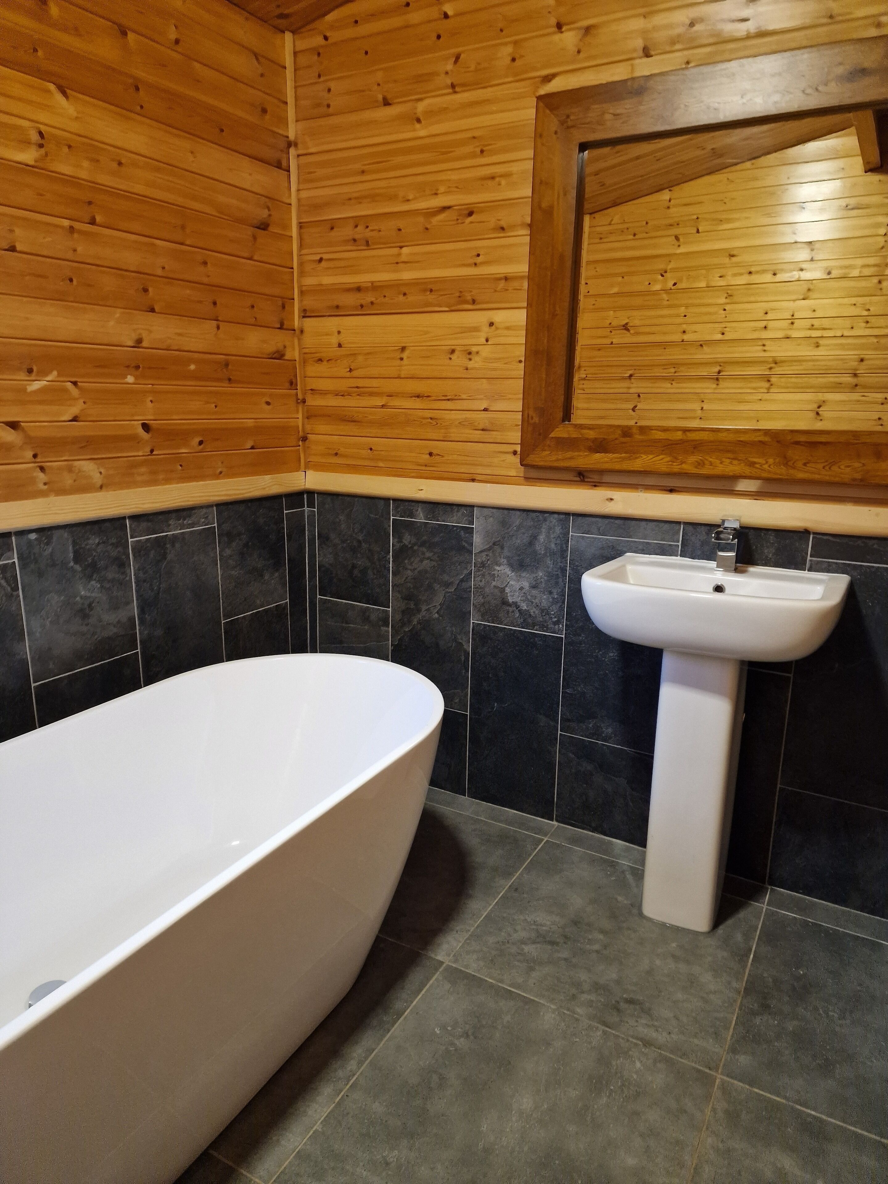 A bathroom with a wooden wall, a white bathtub, and a white sink.