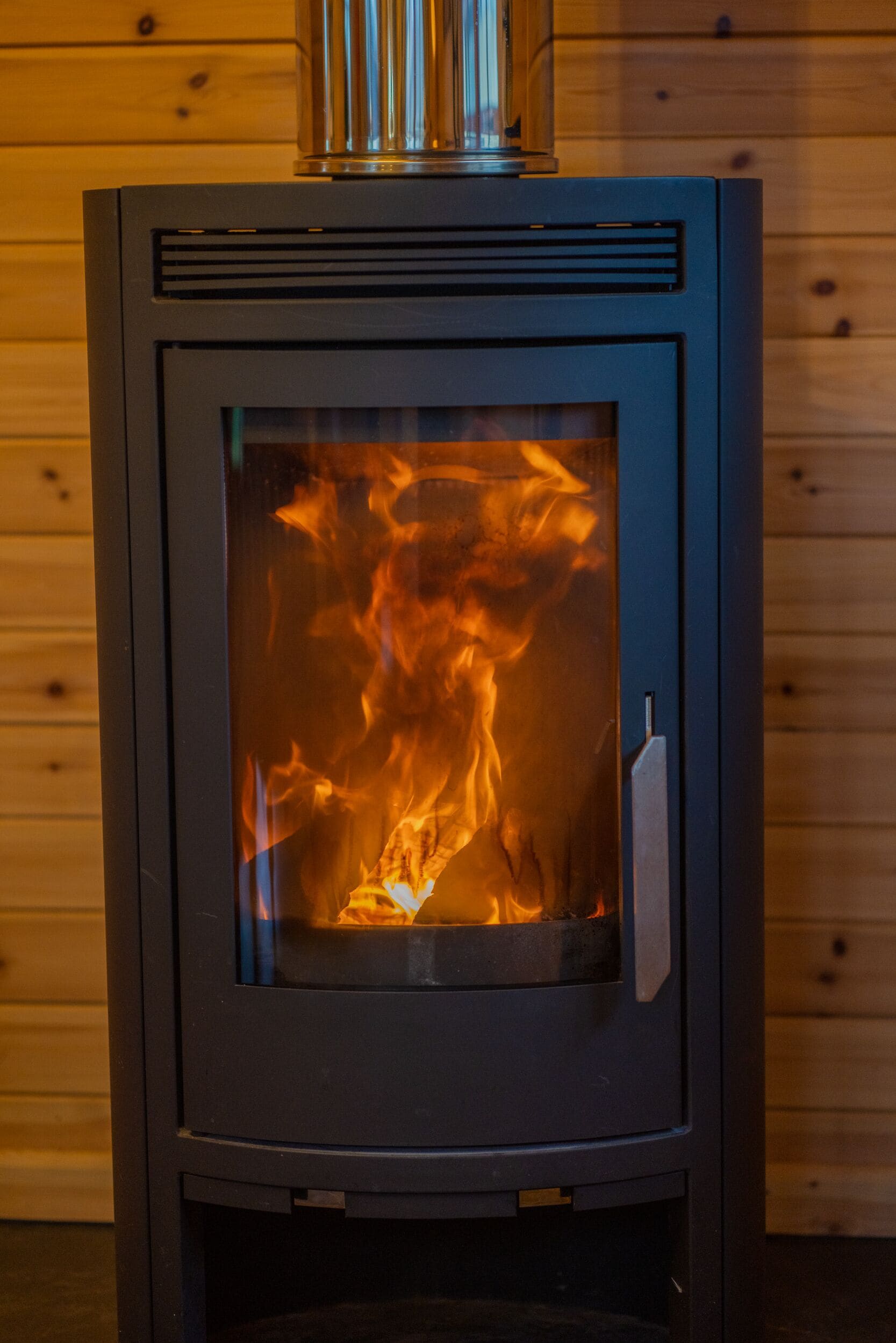 A wood-burning stove with a glass door, set against a wooden wall background.
