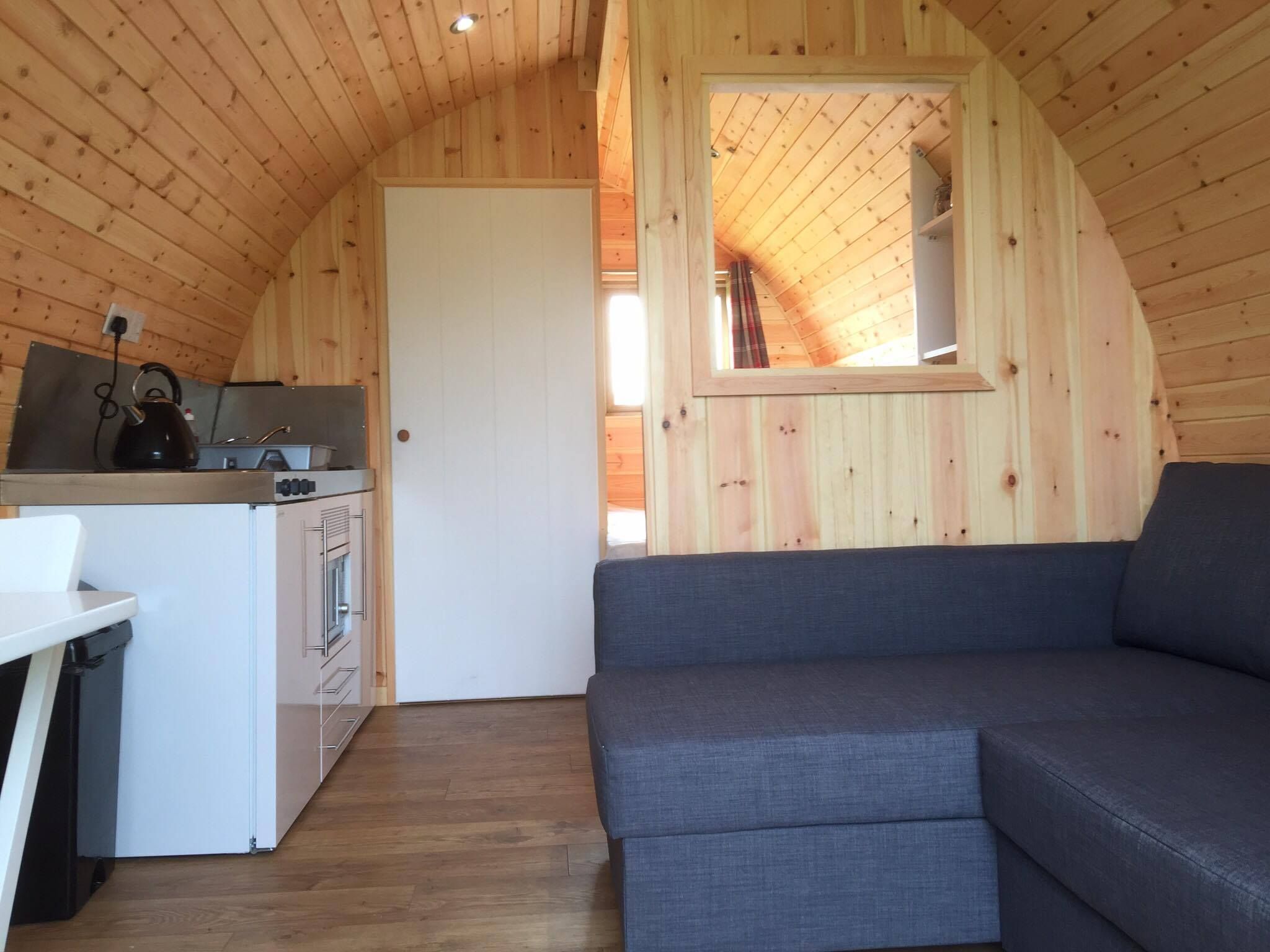 A cozy cabin interior with a kitchenette, a gray sofa, and a wooden ceiling.