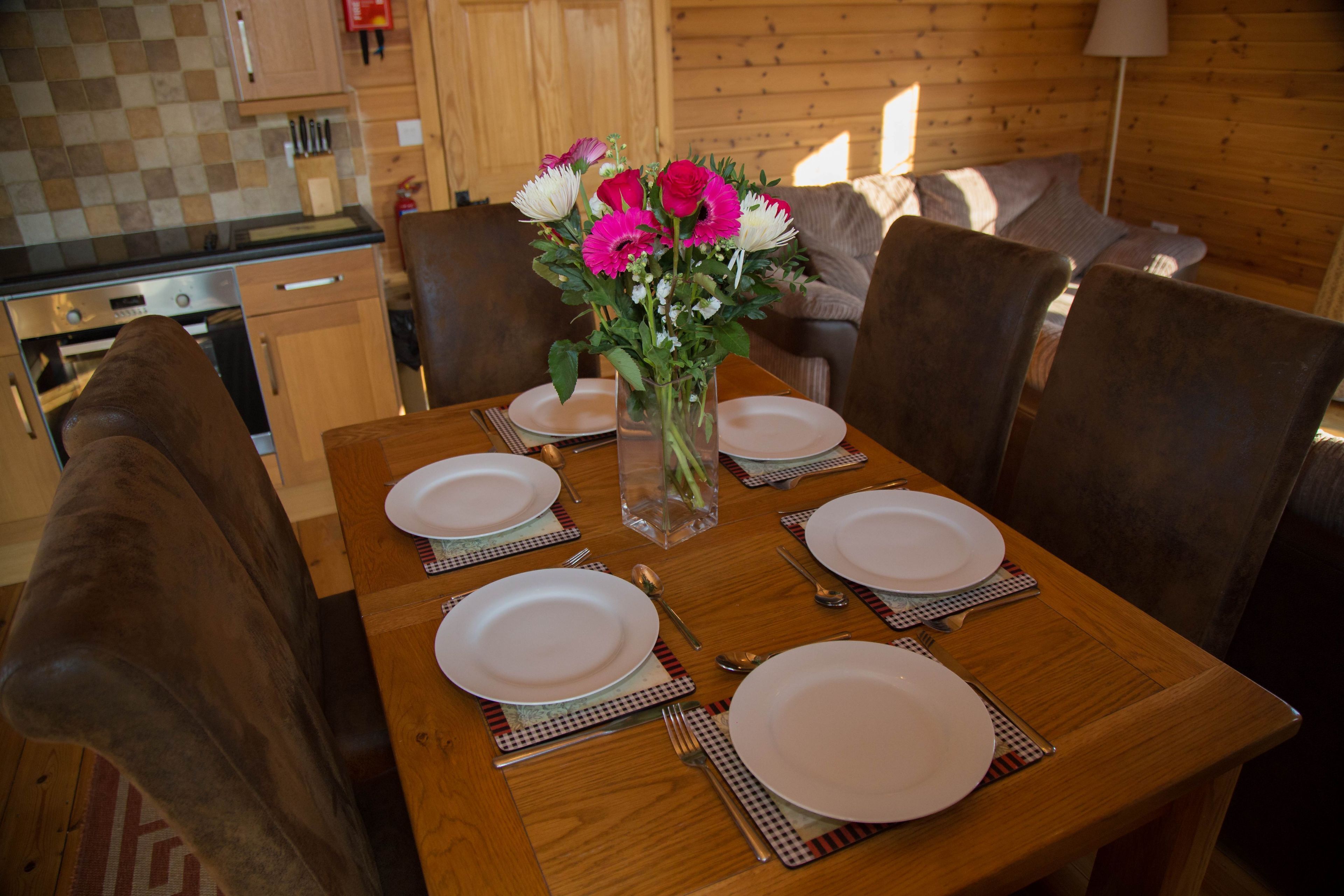 A dining table set with plates, cutlery, and a vase of flowers in a wooden interior.