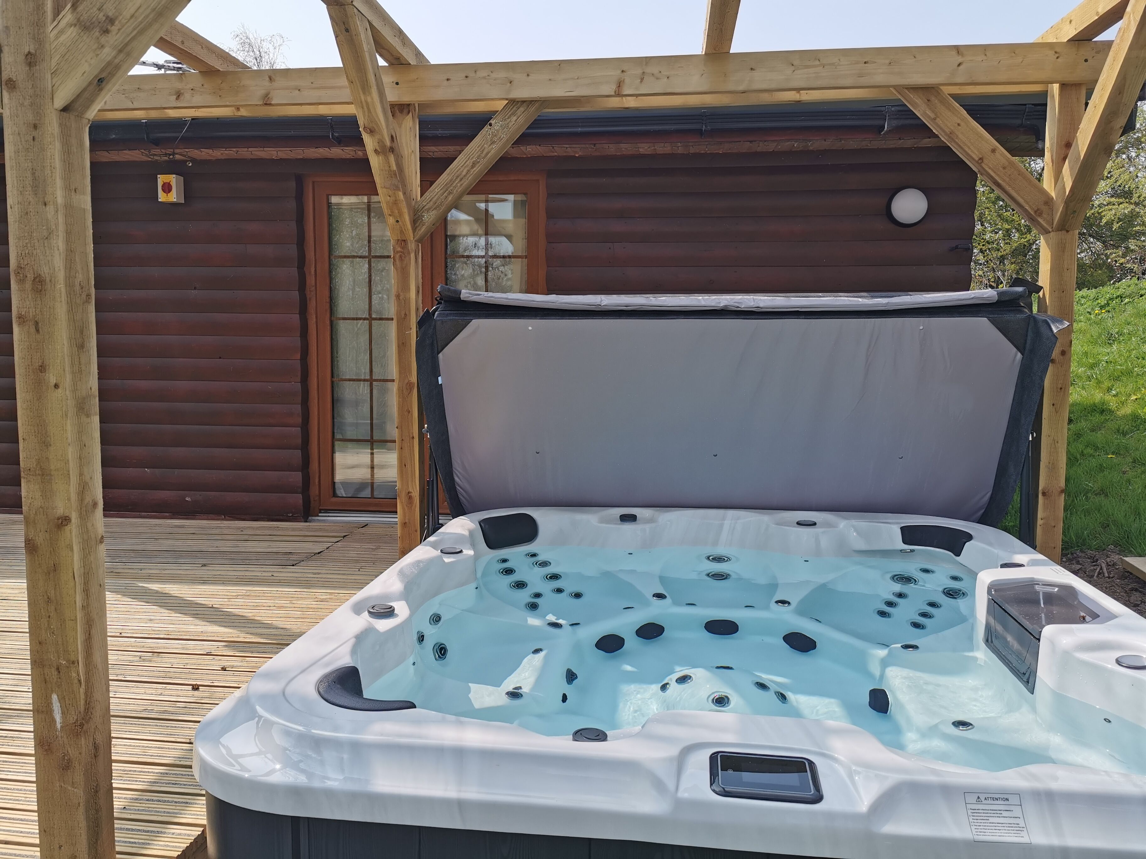 A hot tub in a wooden deck area with a wooden cabin in the background.