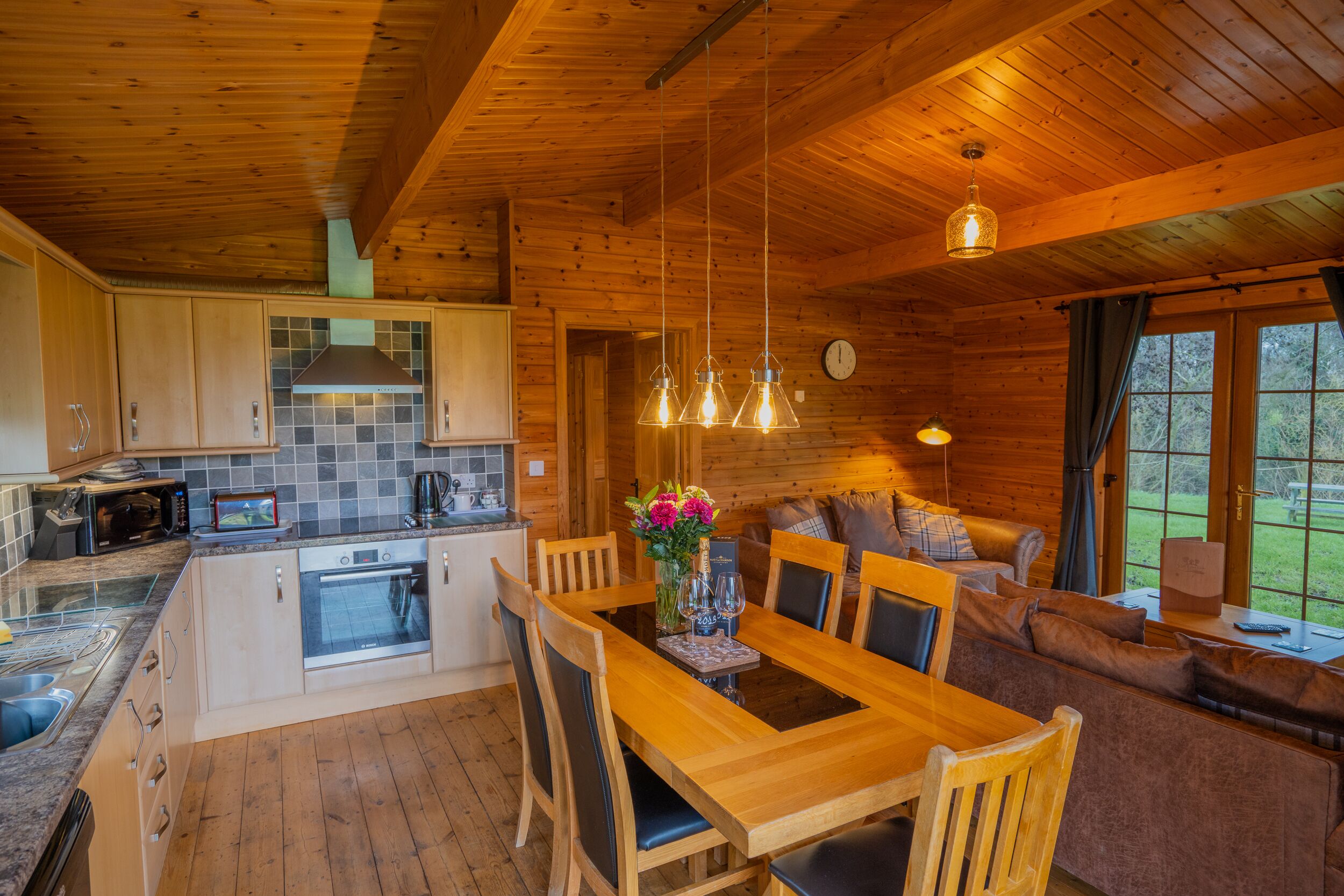 A wooden cabin interior with a kitchen, dining area, and living room.
