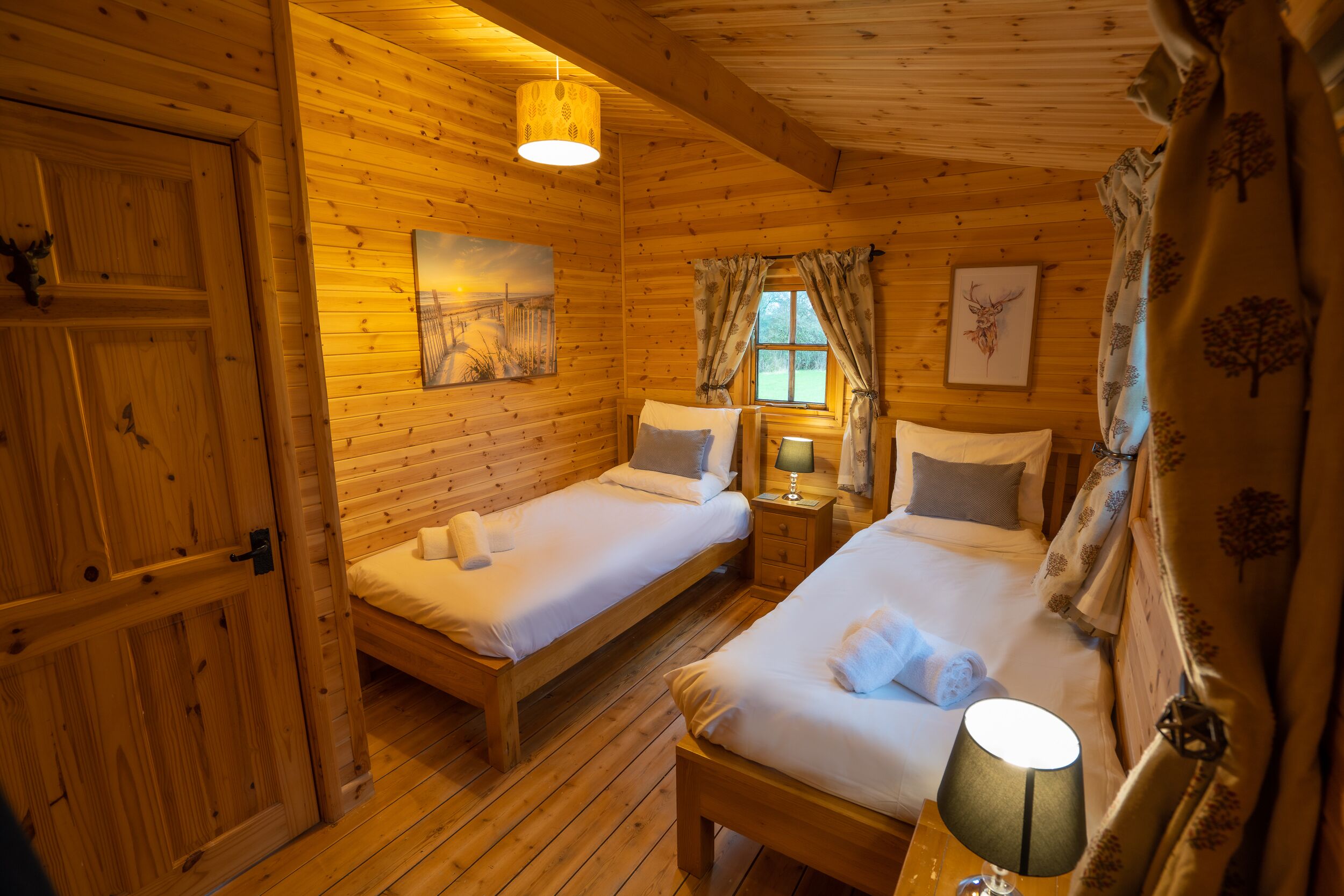 Um quarto de cabana de madeira aconchegante, com duas camas, uma janela com cortinas e um quadro na parede.