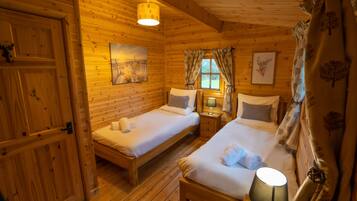 Um quarto de cabana de madeira aconchegante, com duas camas, uma janela com cortinas e um quadro na parede.