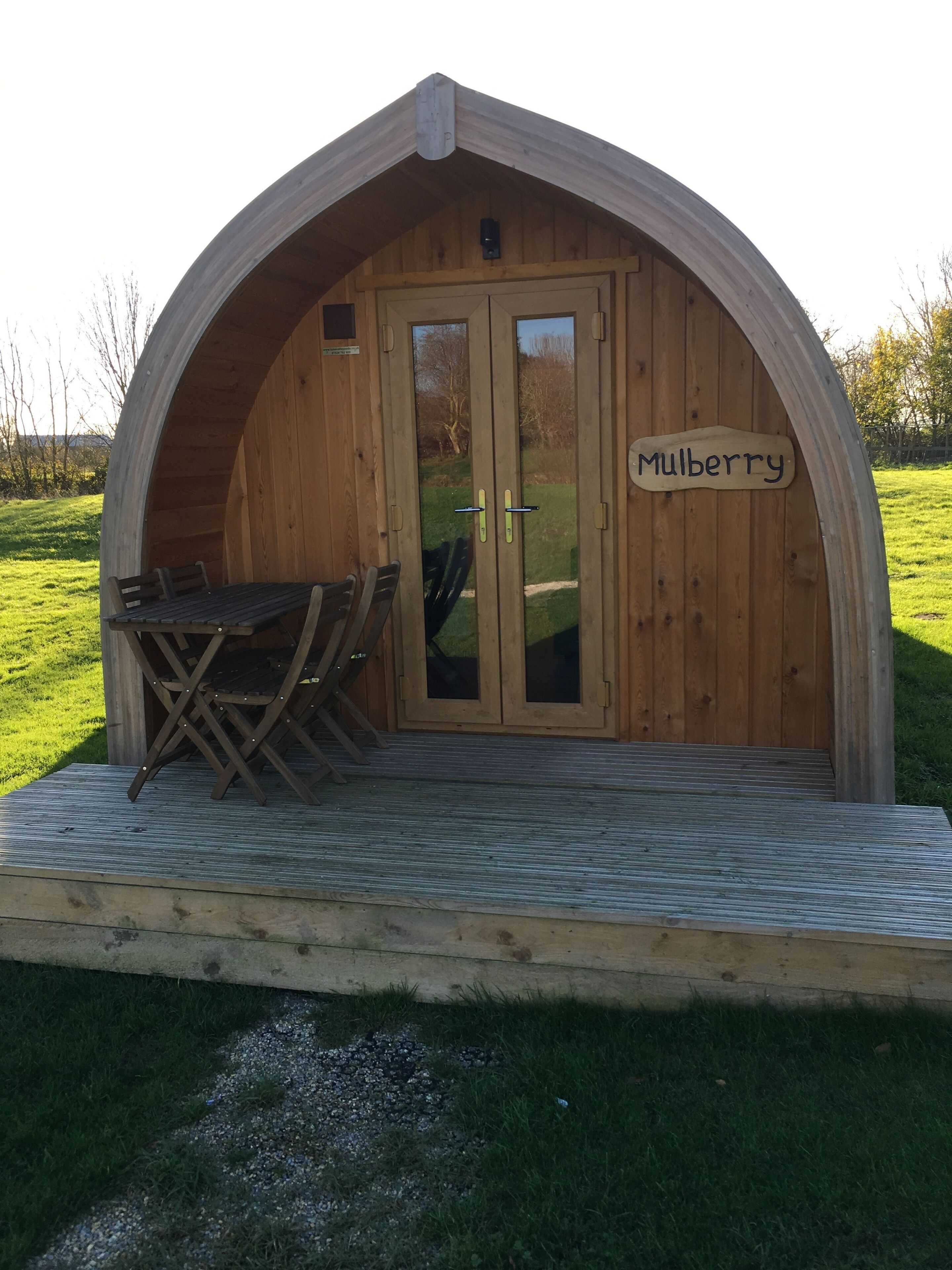 A wooden structure with a sign reading "Mulberry" on the door, a small table, and chairs outside.