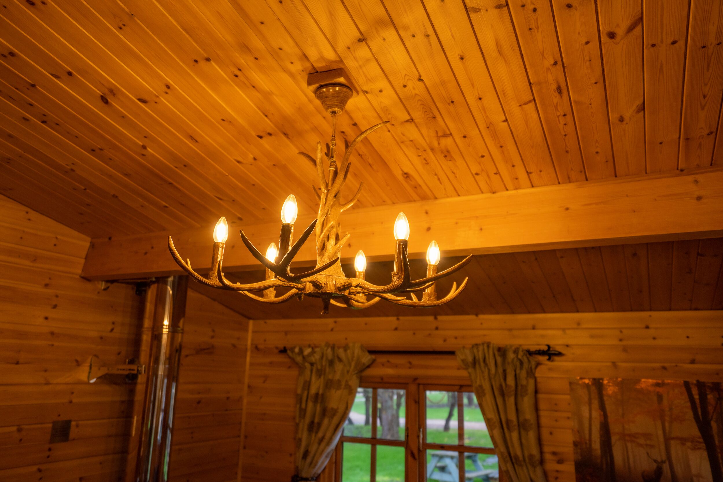 A wooden cabin interior with a chandelier, wooden walls, and curtains.