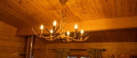 A wooden cabin interior with a chandelier, wooden walls, and curtains.