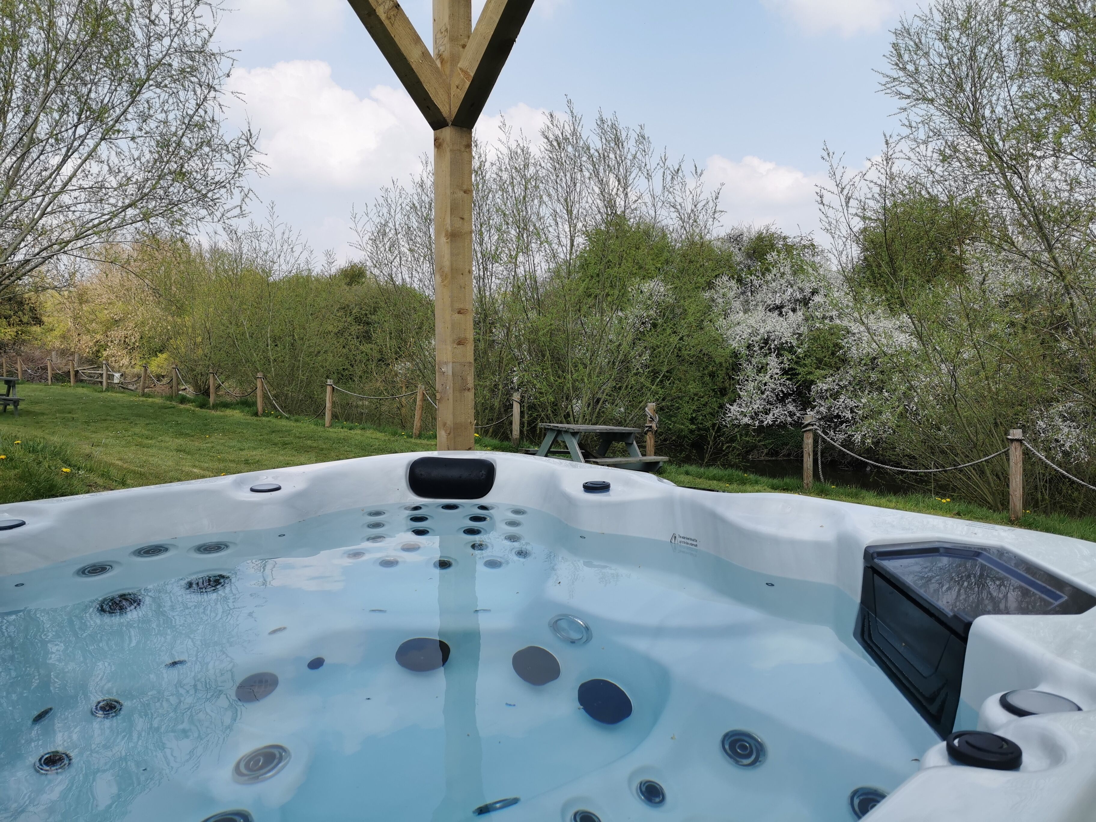 A hot tub with multiple jets, surrounded by a wooden deck and a fence.