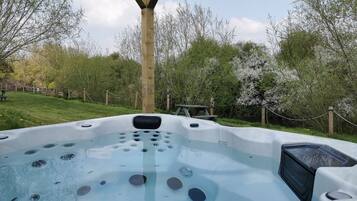 A hot tub with multiple jets, surrounded by a wooden deck and a fence.