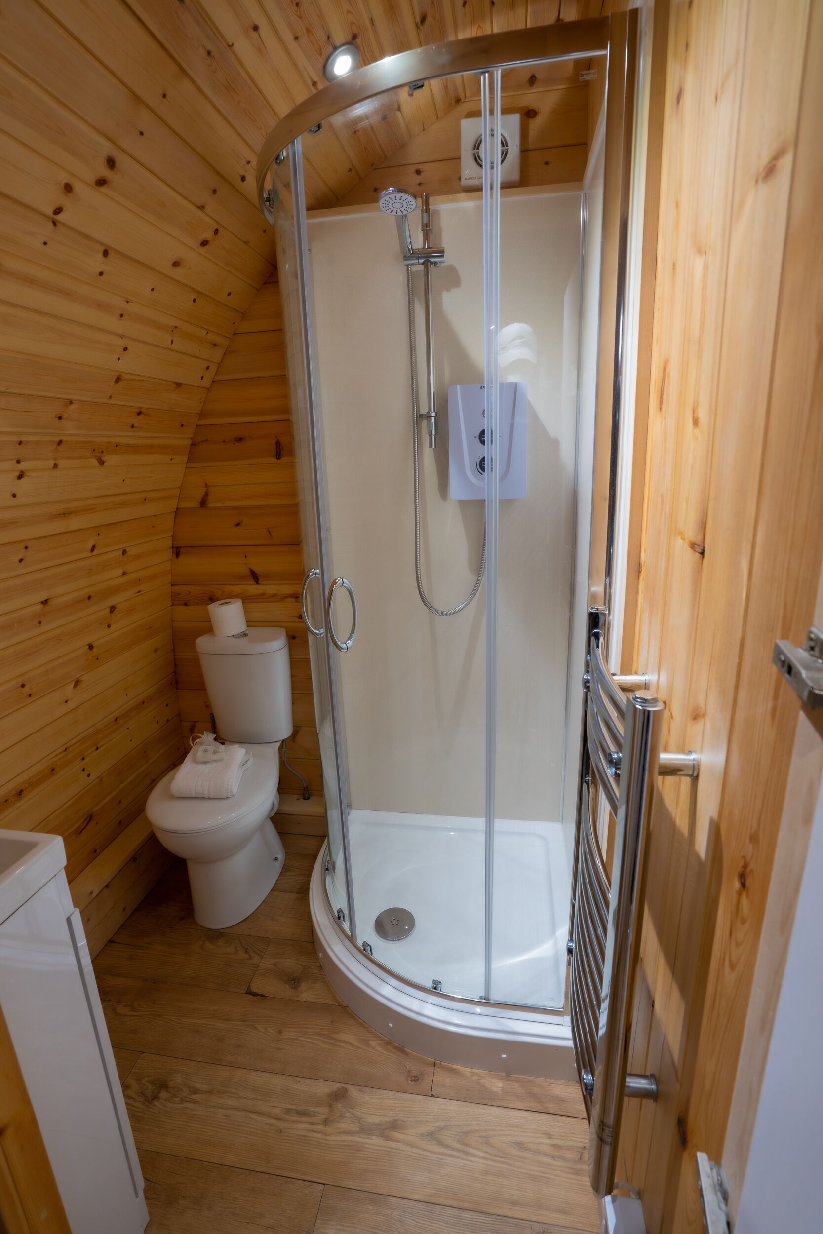 A wooden-paneled bathroom with a glass-enclosed shower, a toilet, and a white sink.