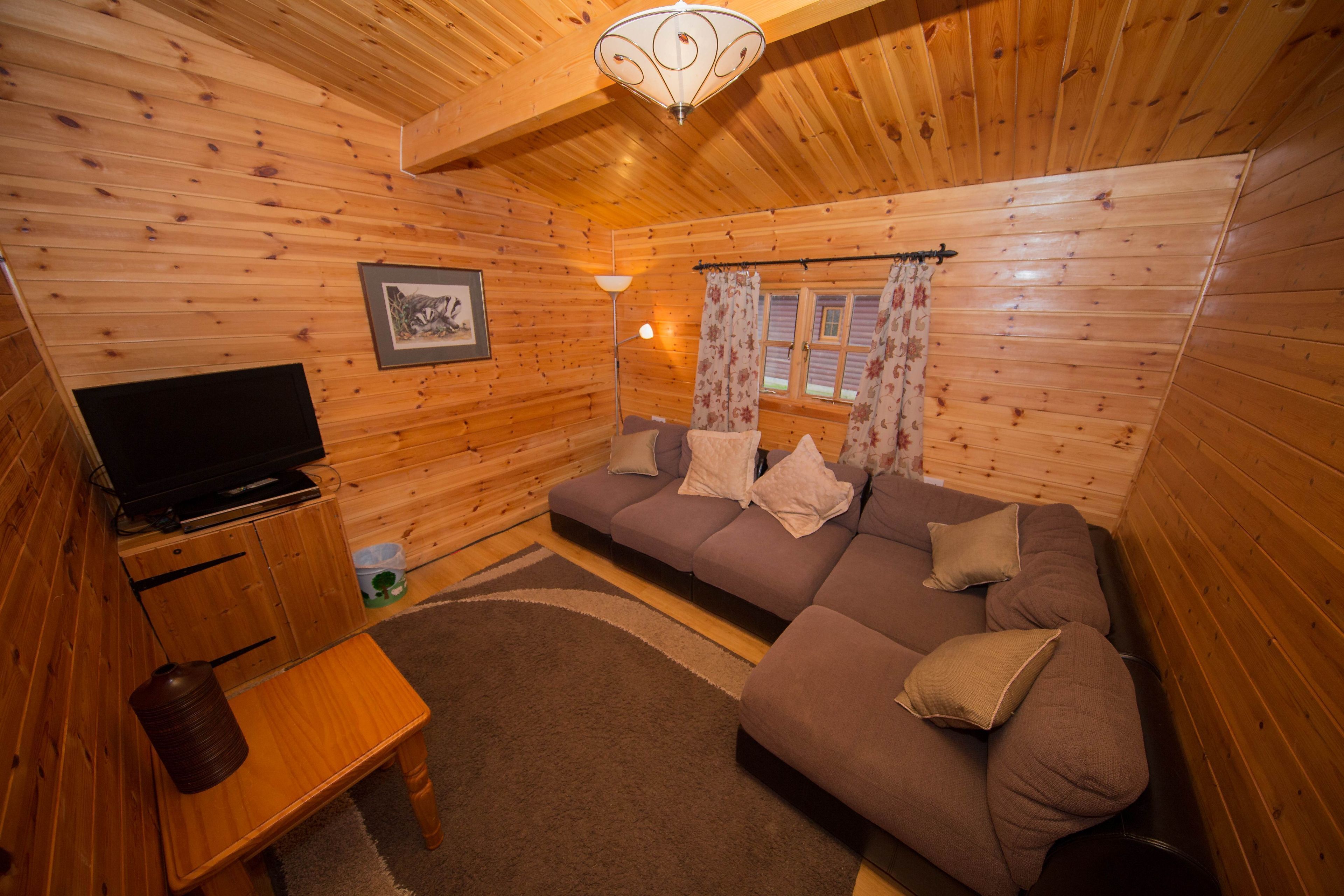 Acogedor interior de cabaña de madera con sofá, televisor y una mesita.