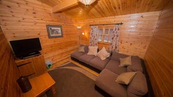 Acogedor interior de cabaña de madera con sofá, televisor y una mesita.