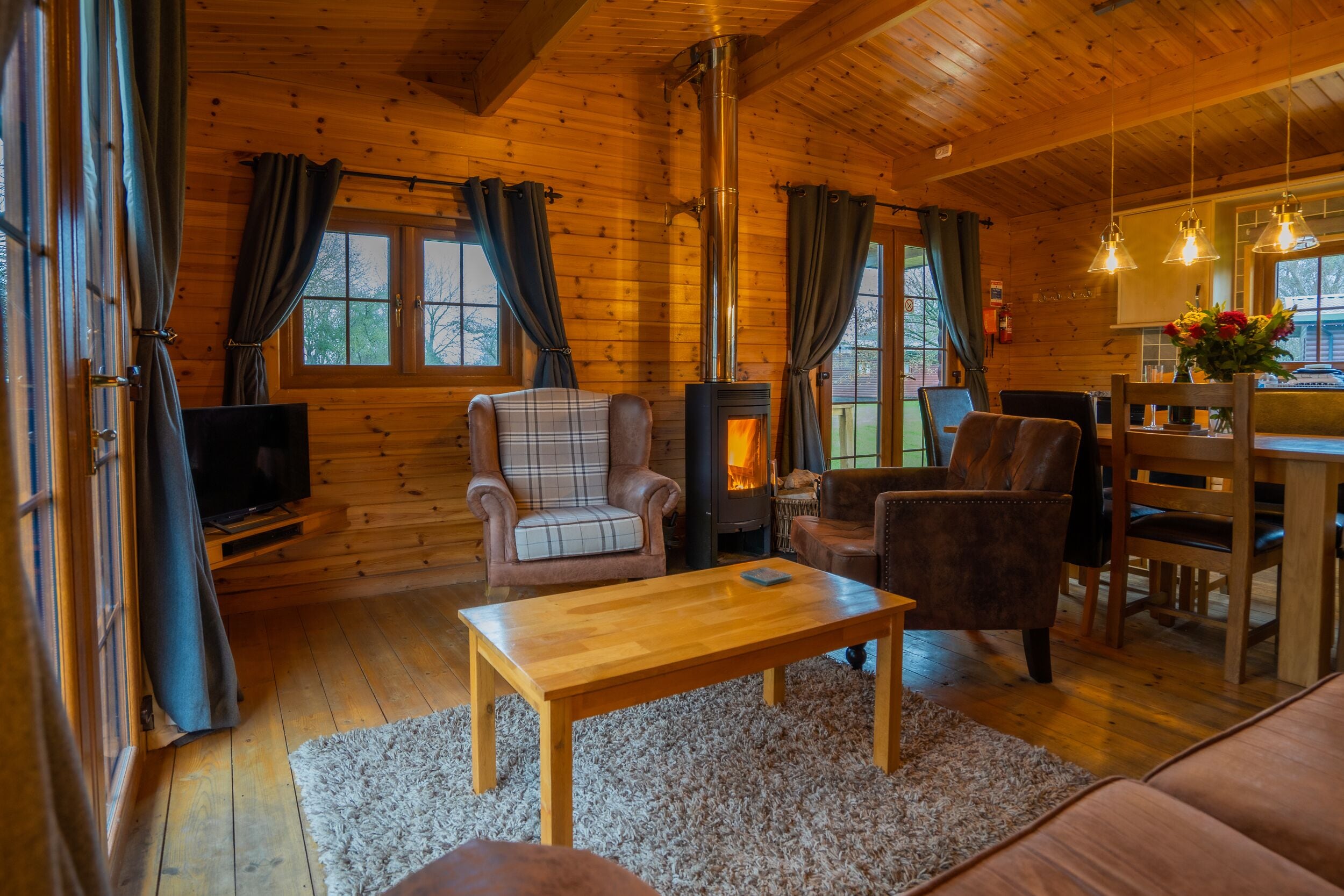 A cozy cabin interior with a fireplace, wooden furniture, and a dining area.
