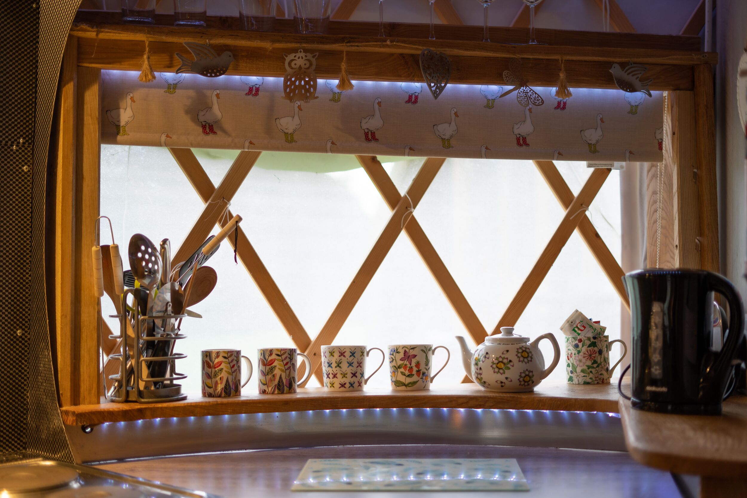 A kitchen window with a view of the outside, a tea set, and various kitchen utensils.