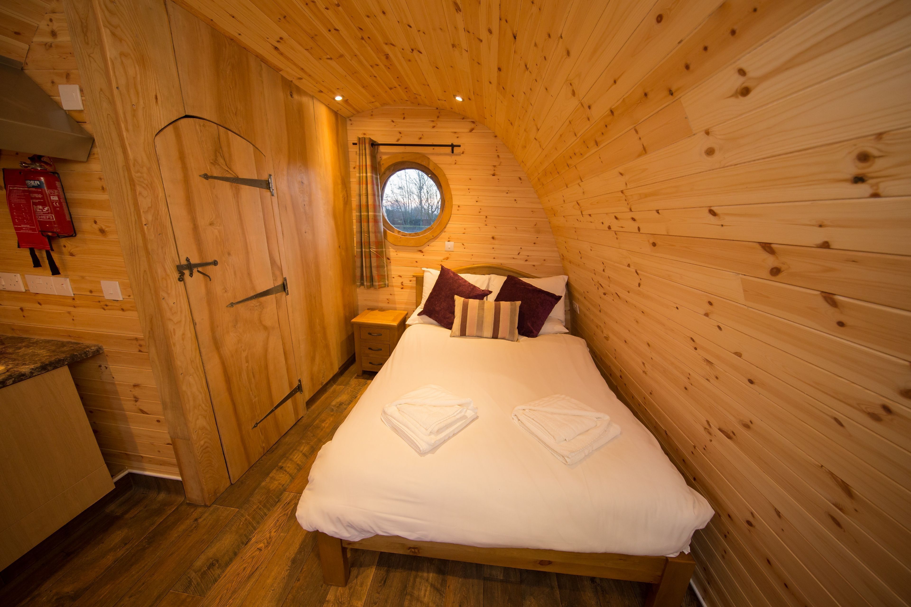 A wooden cabin bedroom with a bed, pillows, and a window.