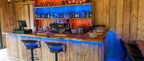 A bar with wooden walls, multiple shelves of liquor bottles, a cash register, and two bar stools.