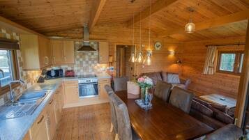 Interior de una cabaña de madera con cocina, comedor y una zona de estar acogedora.