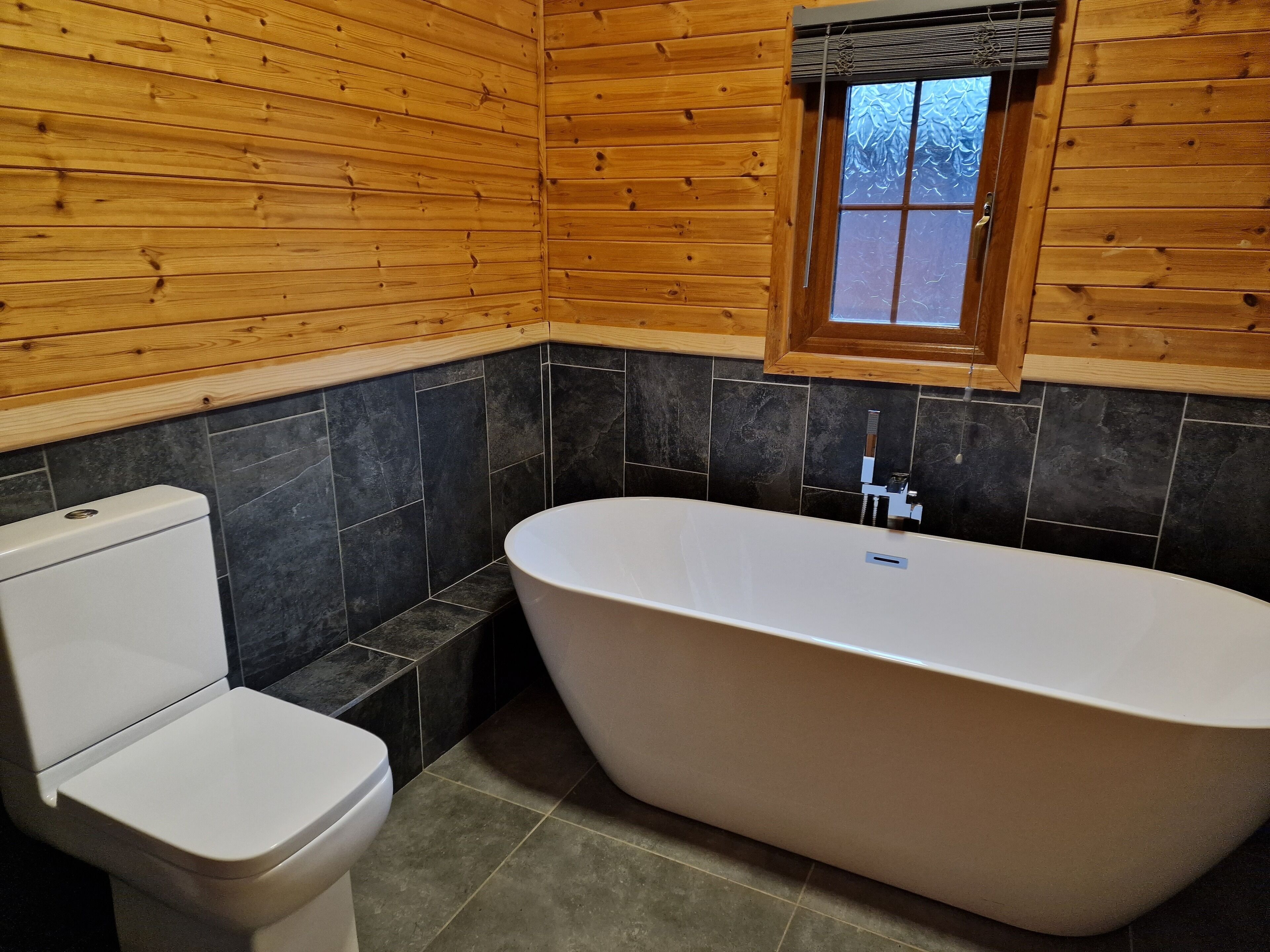 Une salle de bain avec une baignoire sur pieds, des toilettes et une fenêtre en verre dépoli.