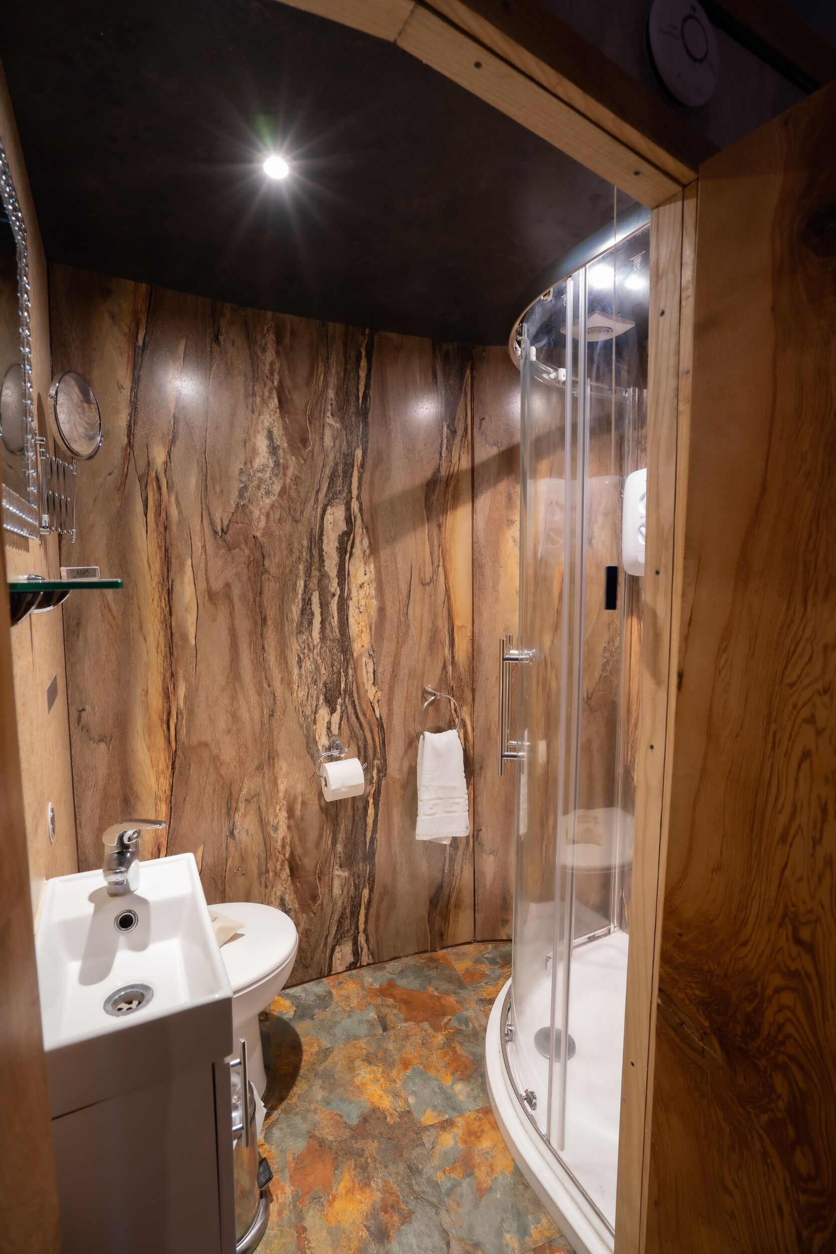 Un baño con pared de mármol, lavamanos, inodoro y ducha con mampara de vidrio.