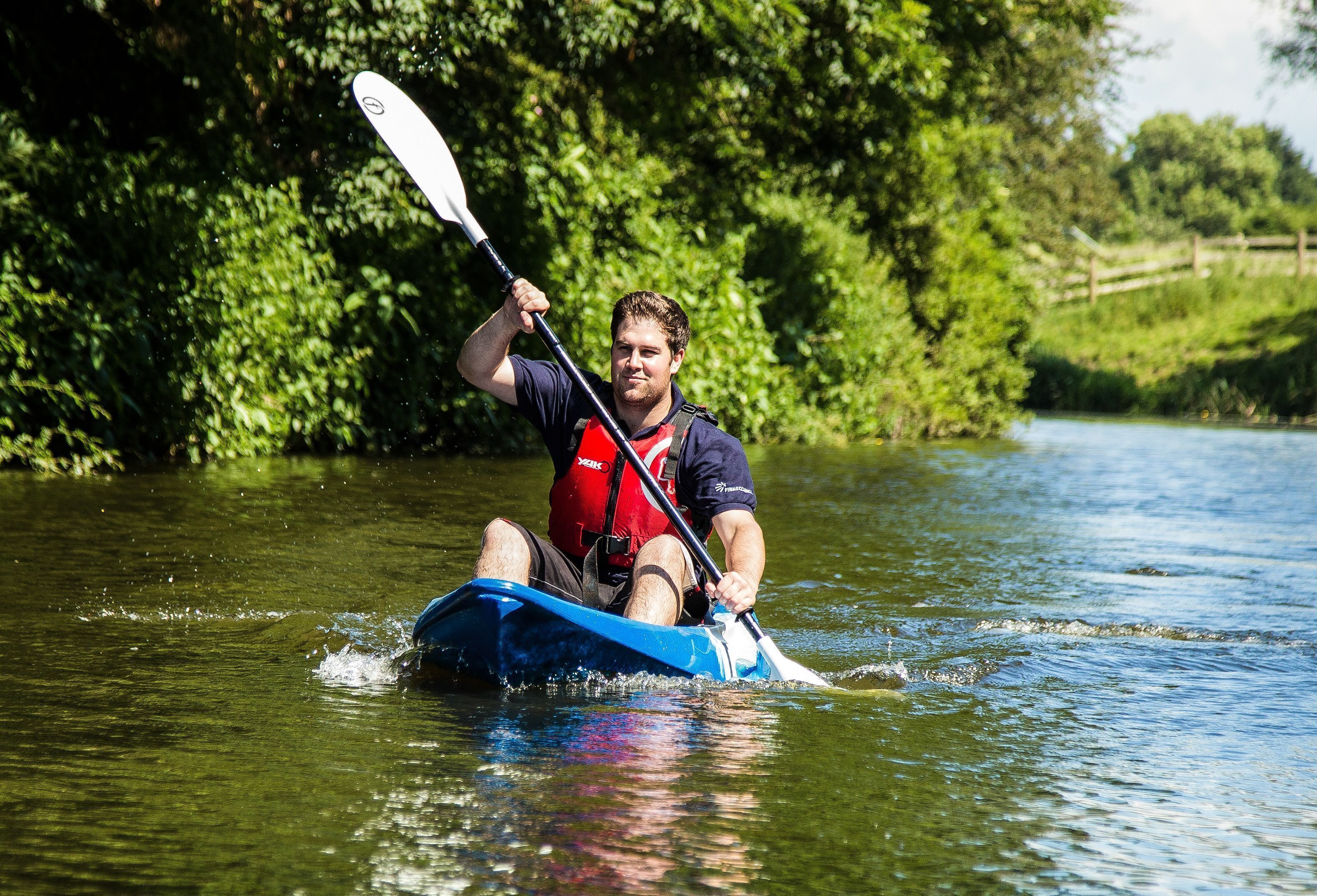 Iemand kajakt op een rivier, omringd door groen.