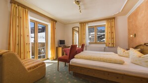 Una habitación de hotel con cama, una silla, un escritorio con ordenador y una ventana con cortinas.