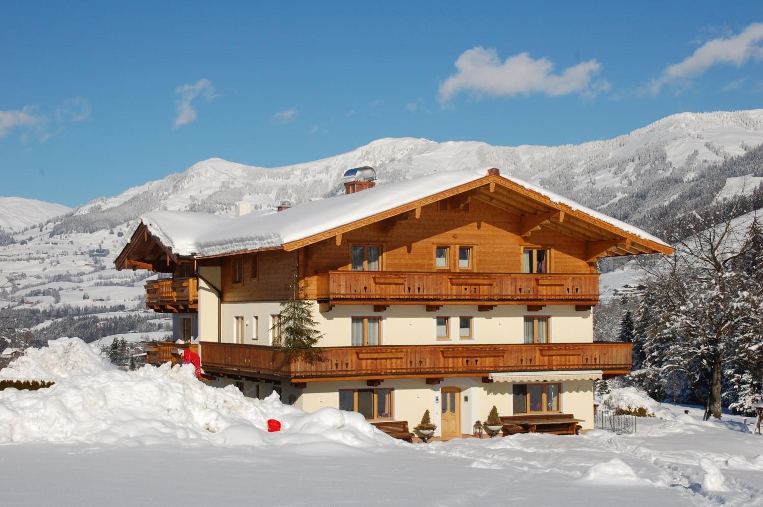 A multi-story wooden chalet with balconies, set against a snowy mountain backdrop.