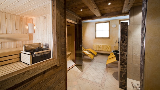 Una sauna de madera con bancos y una puerta de vidrio que da a una zona con baldosas y más bancos.