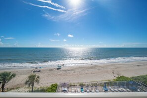 A beach view with a lifeguard tower, umbrellas, and lounge chairs. - Oceanfront 2BR Condo 5th Floor Balcony with Beautiful Ocean Views, 502 (Indian Harbour Beach)