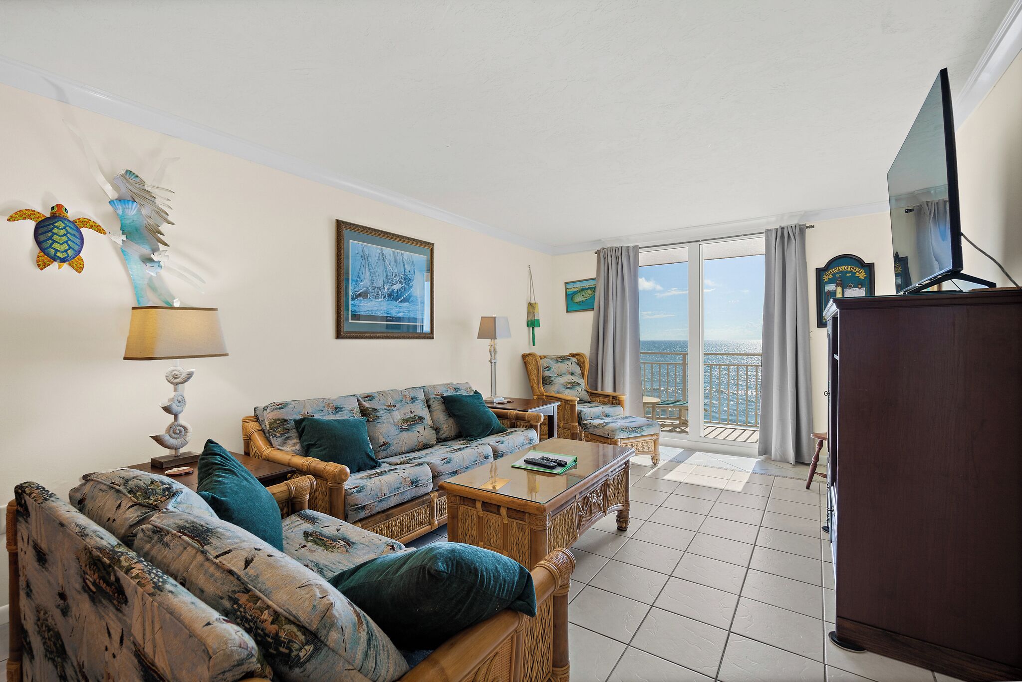 A living room with a sofa, chairs, a coffee table, and a TV. There is a balcony with a view.