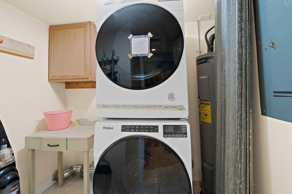 A compact laundry area with a stacked washer and dryer, a wooden cabinet, and a small table with a pink basin. - Oceanfront 2BR Condo 5th Floor Balcony with Beautiful Ocean Views, 502 (Indian Harbour Beach)