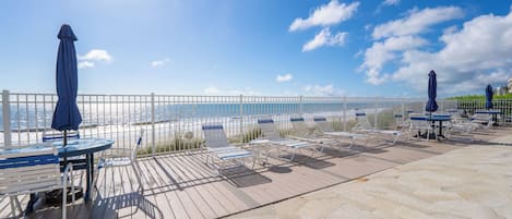 A deck with outdoor seating, a railing, and a view of the ocean.