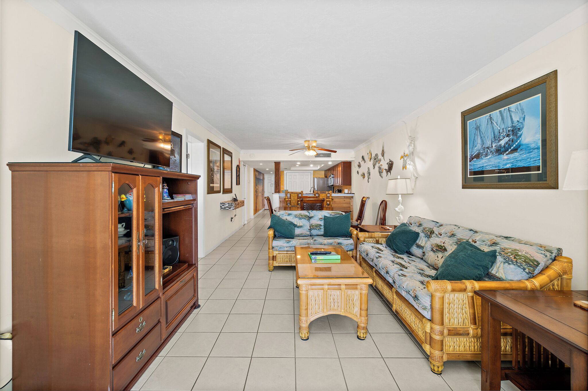 A spacious living room with a large flat-screen TV, a wooden cabinet, a sofa with cushions, and a dining area with a table and chairs.