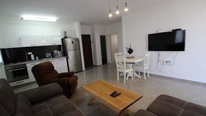 A modern living room with a sofa, a wooden coffee table, and a TV mounted on the wall. - Arendalzrail Apartments Khana Szenes St. (Bat Yam)