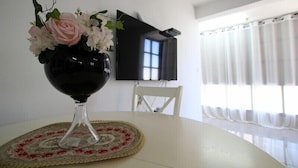 A dining table with a vase of flowers, a placemat, a chair, and a TV mounted on the wall. - Arendalzrail Apartments Khana Szenes St. (Bat Yam)