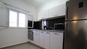A modern kitchen with stainless steel appliances, white cabinetry, and a window providing natural light. - Arendalzrail Apartments Khana Szenes St. (Bat Yam)