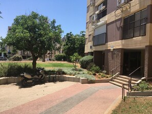 A residential building with a paved entrance, a tree, and a parked motorcycle. - Arendalzrail Apartment - Hertsel St. 4 (Bat Yam)