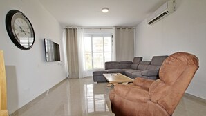 A modern living room with a brown leather sofa, a wooden coffee table, and a flat-screen TV mounted on the wall. - Arendalzrail Apartment - Hertsel St. 4 (Bat Yam)