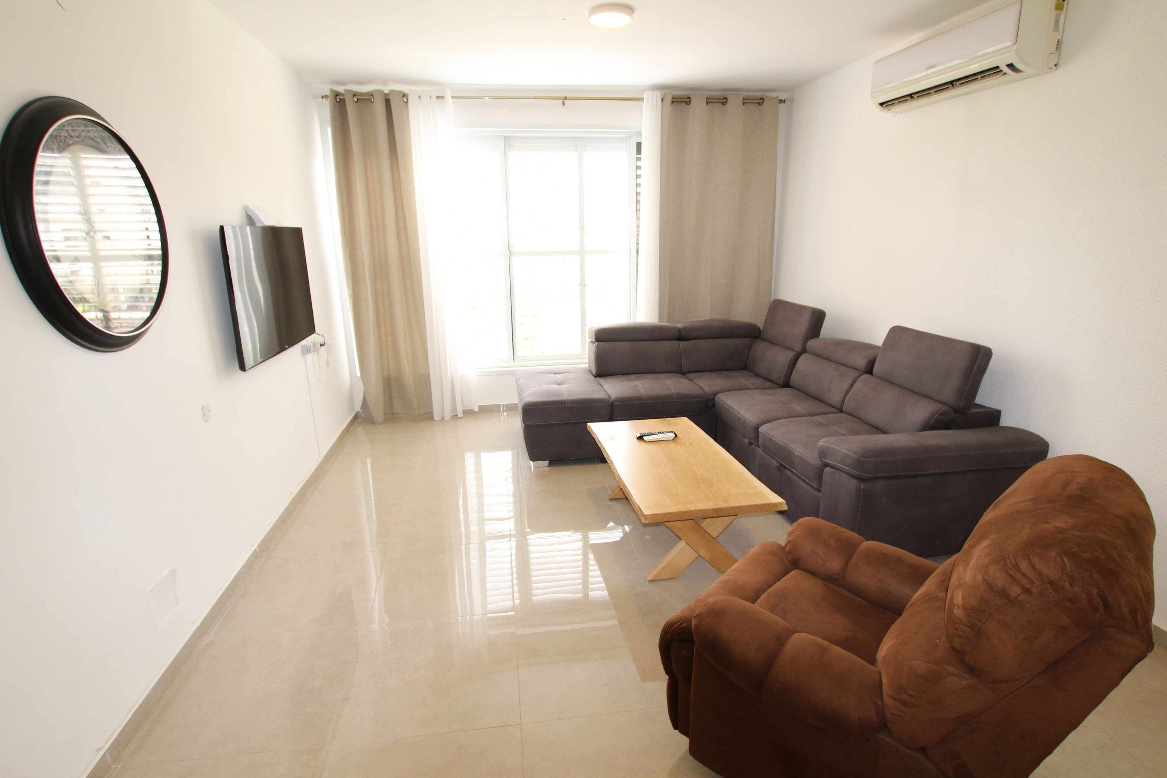 A modern living room with a sectional sofa, a wooden coffee table, and a brown armchair.